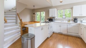A modern kitchen with white cabinetry, a wooden staircase, and a view of the outdoors through large windows. - Secluded Creekside Home | Incredible Views | A/C | Private Deck | STR2025-036 (Ridgway)
