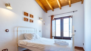 Un lit simple dans une chambre avec un plafond en pente, une fenêtre avec des rideaux et des lampes fixées au mur.