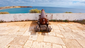 Un canon est installé sur une plateforme en pierre, surplombant une zone côtière sous un ciel dégagé.