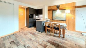 A compact kitchen with a dining area, wooden flooring, and a large window with a view.