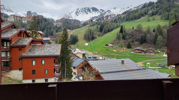 A mountainous village with traditional wooden buildings, a ski slope, and snow-capped peaks in the background.
