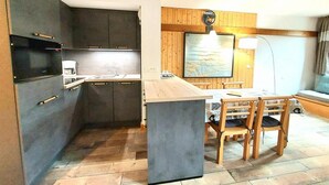 A compact kitchen with dark cabinets, a wooden island, and a dining area with chairs and a table.