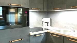 A modern kitchen with dark cabinets, a built-in oven, a coffee maker, and a sink.