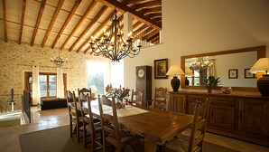 Un espace repas avec une table et des chaises en bois, un lustre et des murs en pierre.