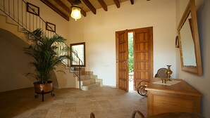 Une pièce spacieuse avec un escalier, une porte en bois donnant sur l’extérieur, un bureau avec une lampe et une plante en pot.