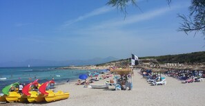 A beach with rows of yellow paddle boats, a flag, and people relaxing on the sand.