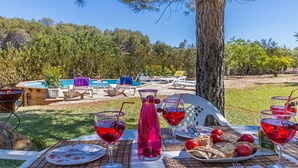 Un área de comedor al aire libre con una mesa preparada para una comida, rodeada por una piscina y sillas de descanso.