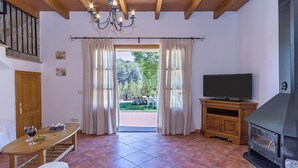 Una sala de estar acogedora con un mueble bajo de madera para el televisor, una chimenea, una mesa de comedor con sillas y vistas al jardín a través de la puerta abierta.