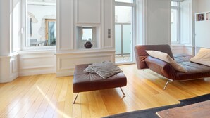 A modern living room with a brown leather sofa, a matching ottoman, and a large window providing natural light.