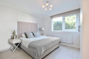 Ein Schlafzimmer mit Bett, Nachttisch, Lampe, Fenster und Heizkörper.