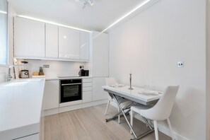 Eine moderne Küche mit weißen Schränken, einem Einbauofen und einem Essbereich mit weißem Tisch und Stühlen.