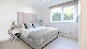 Een moderne slaapkamer met een groot bed, een nachtkastje met lamp en een raam dat natuurlijk licht binnenlaat.