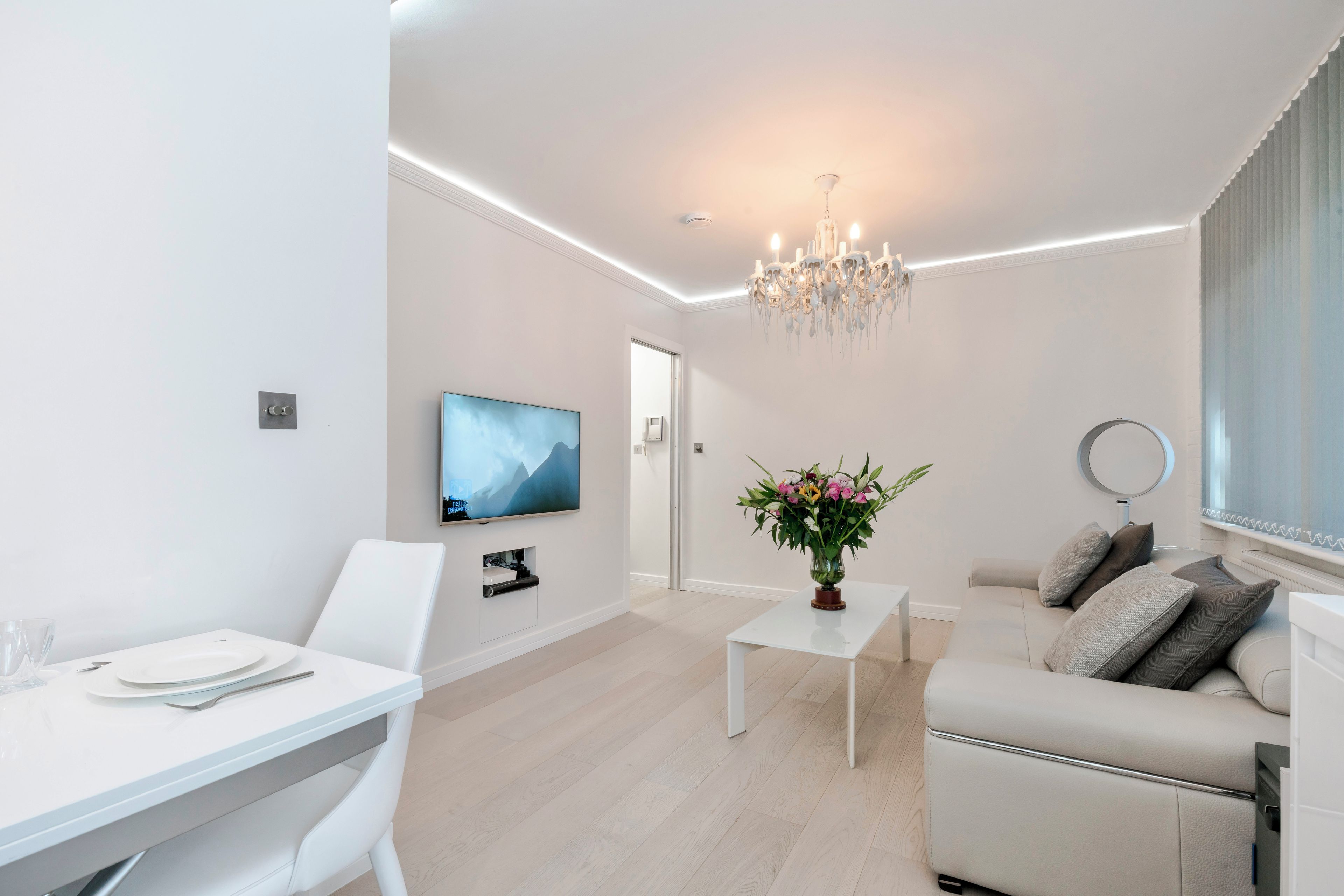 A modern living room with a flat-screen TV, a chandelier, a sofa, and a dining table.