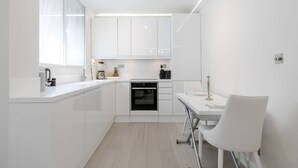 Een moderne keuken met witte kasten, een inbouwoven en een eethoek met een witte tafel en stoel.