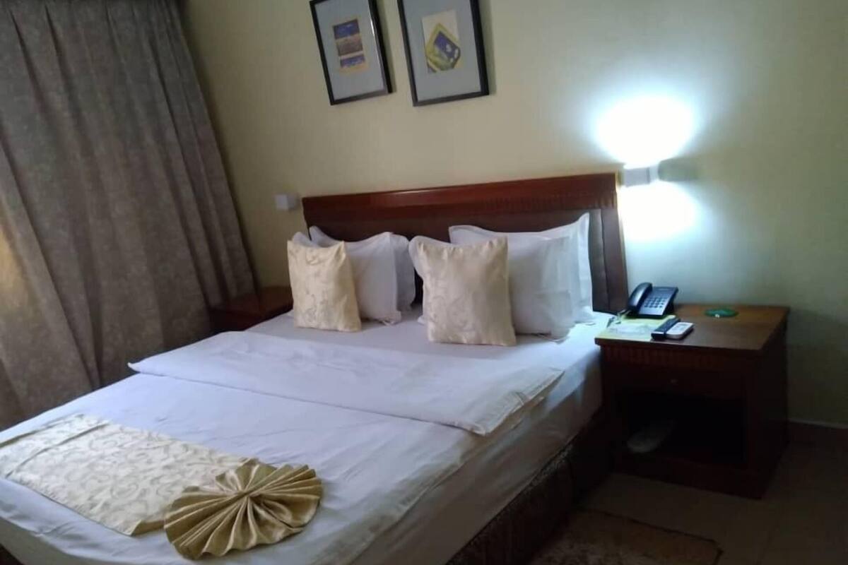 Un lit bien fait, agrémenté d’un coussin décoratif et d’une table de chevet sur laquelle se trouvent une lampe et un téléphone.