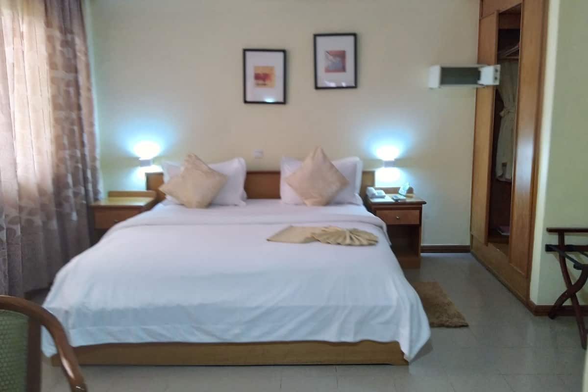 Une chambre d’hôtel avec un lit, deux lampes de chevet, une table de nuit, une porte en bois et un tableau encadré au mur.