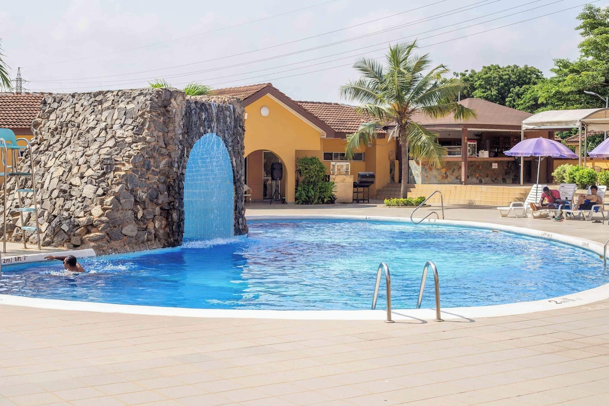 Une piscine agrémentée d’une cascade, de chaises longues et d’un mur en pierre.
