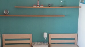 A room with two beds, a small table, a nightstand, a lamp, and a shelf with decorative items. - 2 room vacation apartment Strandpromenade Sankt Peter Ording (Sankt Peter-Ording)