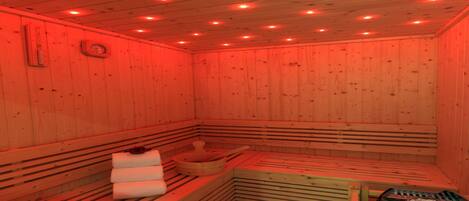 A sauna with wooden walls and benches, a wooden bench with a towel, and a stone basin.