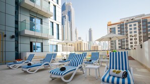 Terraza en la azotea con tumbonas y sombrillas, con vistas a un paisaje urbano de edificios modernos.