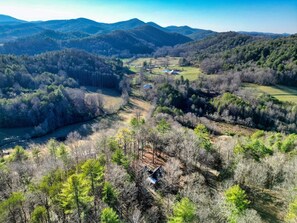 Un paysage rural avec une petite cabane entourée d’une forêt dense et de collines ondulantes.