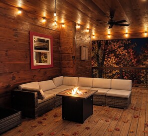 A wooden deck with a fire pit, a sofa, and a ceiling fan.