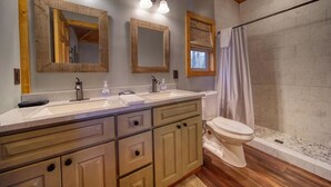 Une salle de bain avec un meuble-lavabo en bois, deux vasques, des toilettes et une douche avec un rideau.