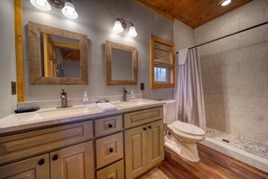 Une salle de bain avec un meuble-lavabo en bois, deux vasques, des toilettes et une douche avec un rideau.