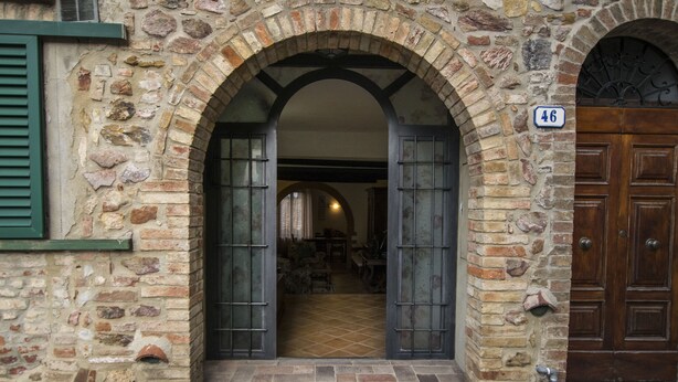 Un bâtiment en pierre doté d’une grande porte d’entrée en arc de cercle, d’une porte en bois avec une plaque numérotée et d’un sol carrelé.