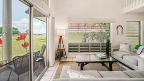Amplia sala de estar con un gran ventanal corredera que da a un balcón, un sofá, una mesa de centro y una lámpara de pie.