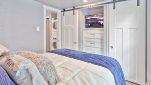 Un dormitorio con cama, cómoda, lavadora y armario corredero.