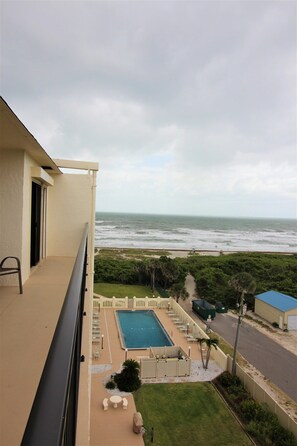 A balcony with a view of the ocean, a swimming pool, and a small garden area.