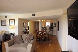 A living room with a sofa, a dining area with chairs and a table, and a kitchen in the background.