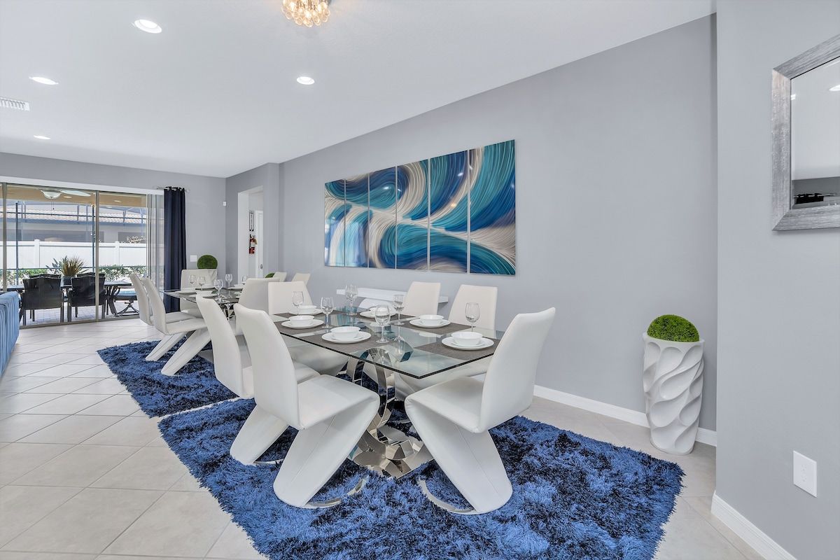 A modern dining area with a glass table, white chairs, and a blue shag rug.