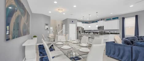 A modern dining area with a glass table and white chairs, a blue shag rug, and a blue sofa in the background.