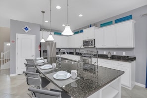 A modern kitchen with white cabinets, a granite countertop, stainless steel appliances, and pendant lighting.