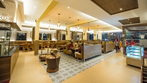 A modern hotel lobby with seating areas, a central decorative feature, and a view of the cityscape. - Hotel Annamalai (Bahur)