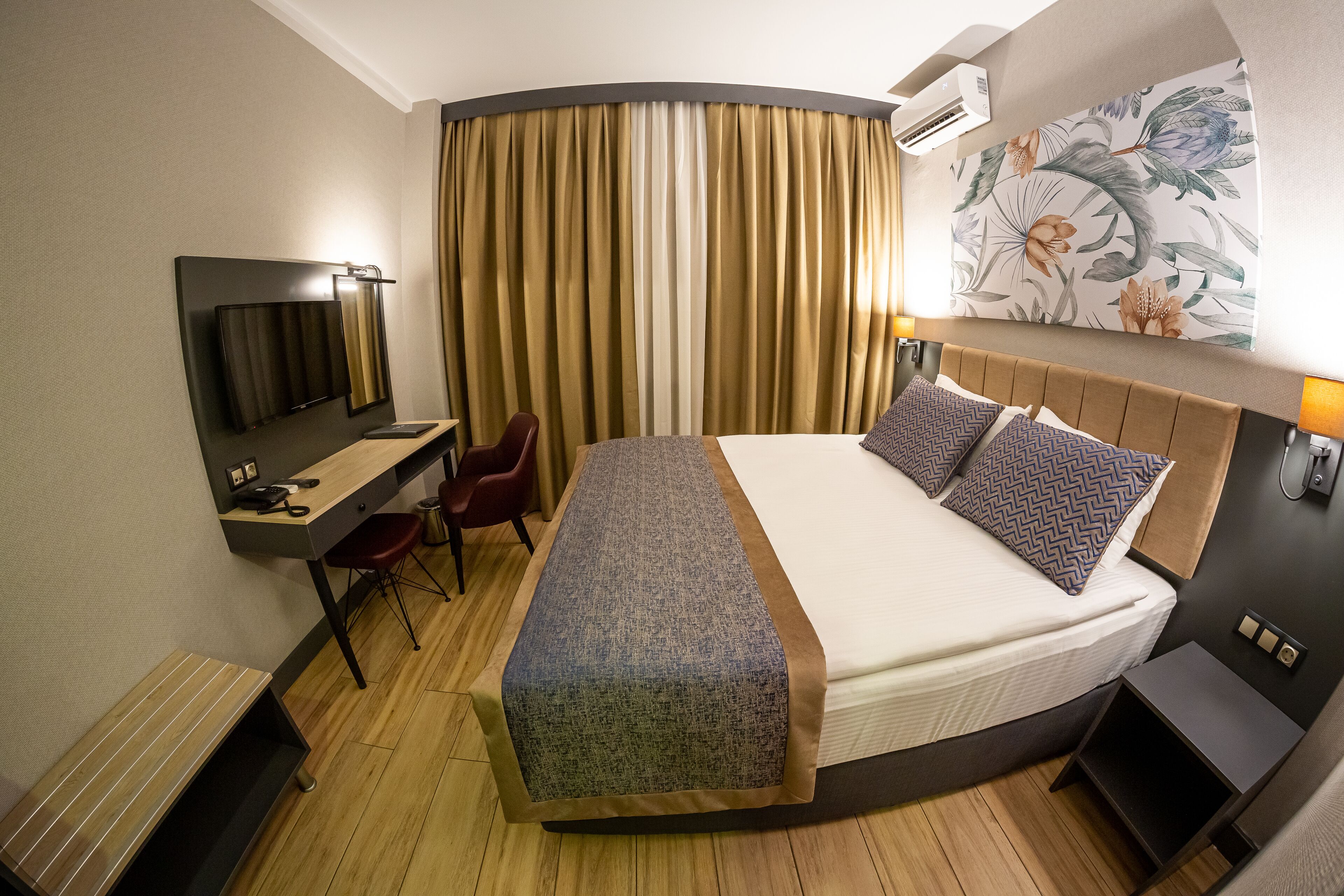 Habitación de hotel con cama, escritorio, silla y un ventanal con cortinas.