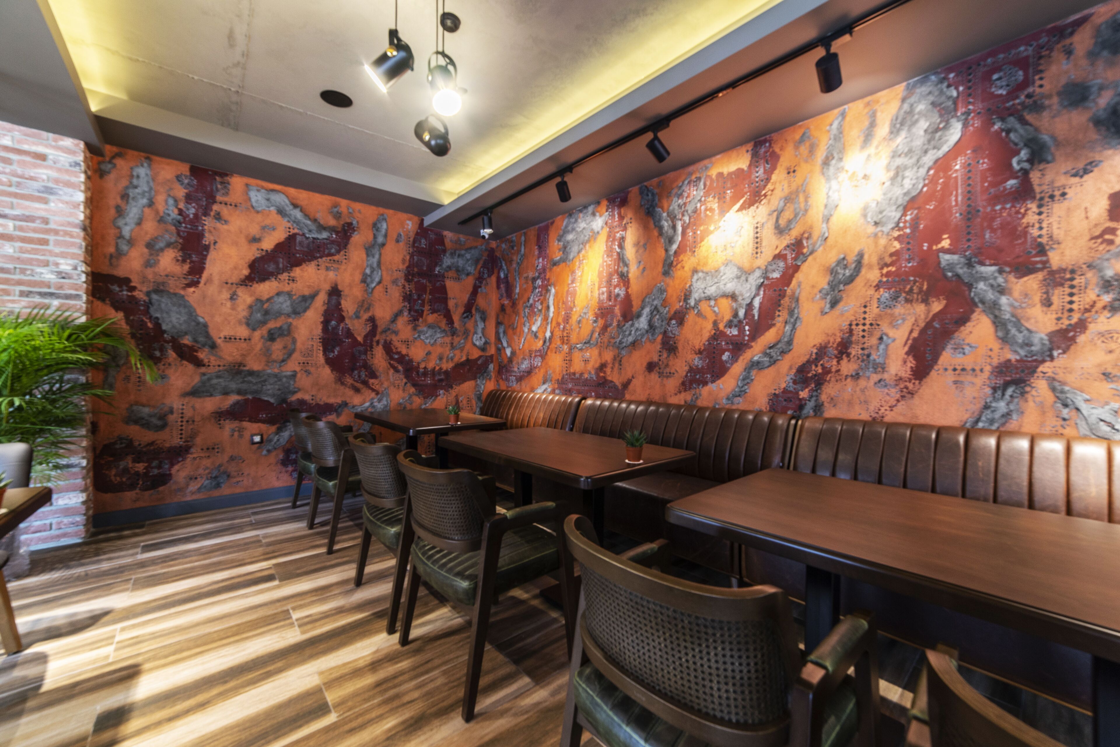 A restaurant interior with wooden flooring, metal wall decor, and seating arrangements.