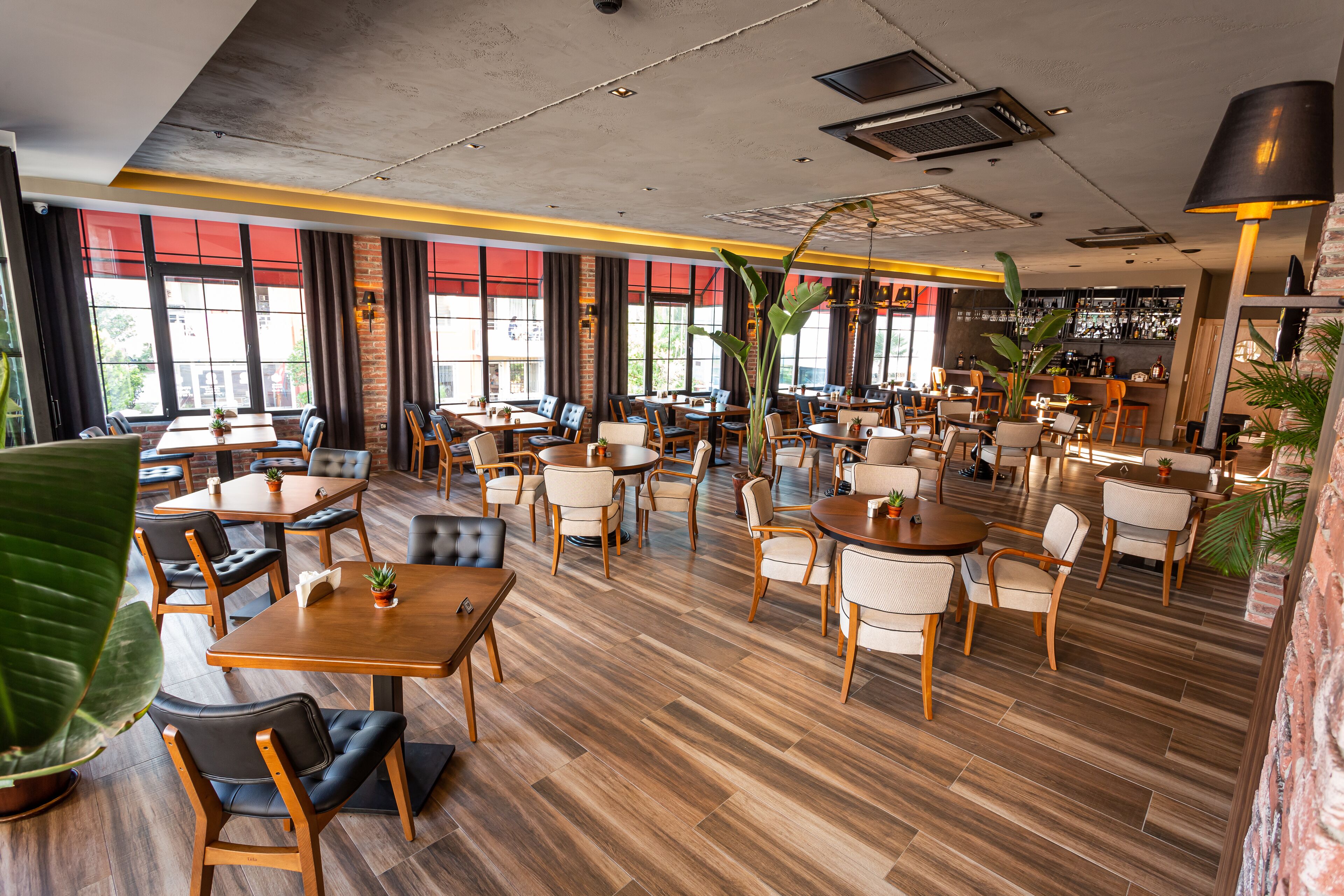 A spacious restaurant with multiple dining areas, wooden tables and chairs, and large windows allowing natural light.