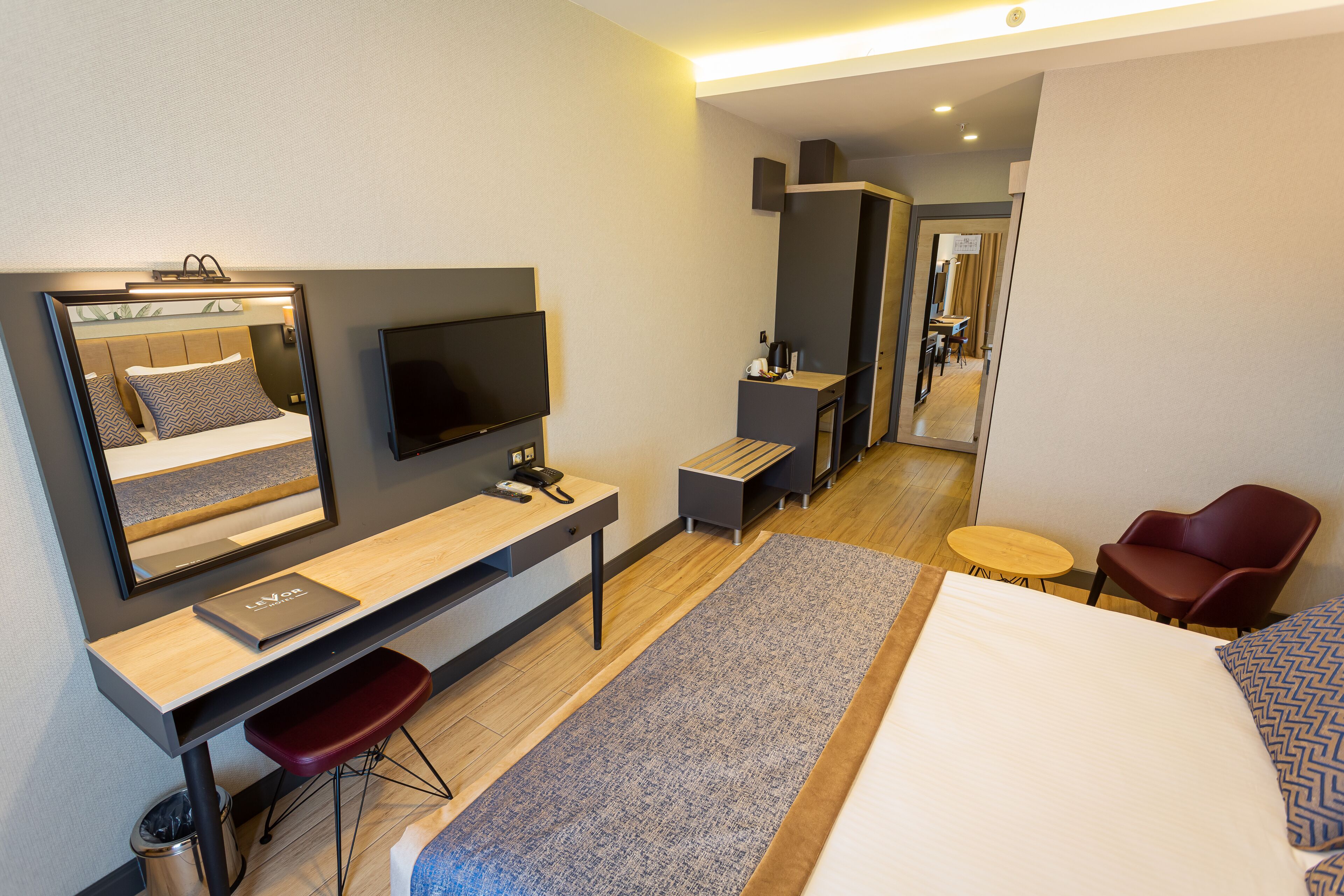 A modern hotel room with a bed, desk, chair, TV, and a mirror.