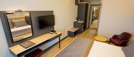 A modern hotel room with a bed, desk, chair, TV, and a mirror.