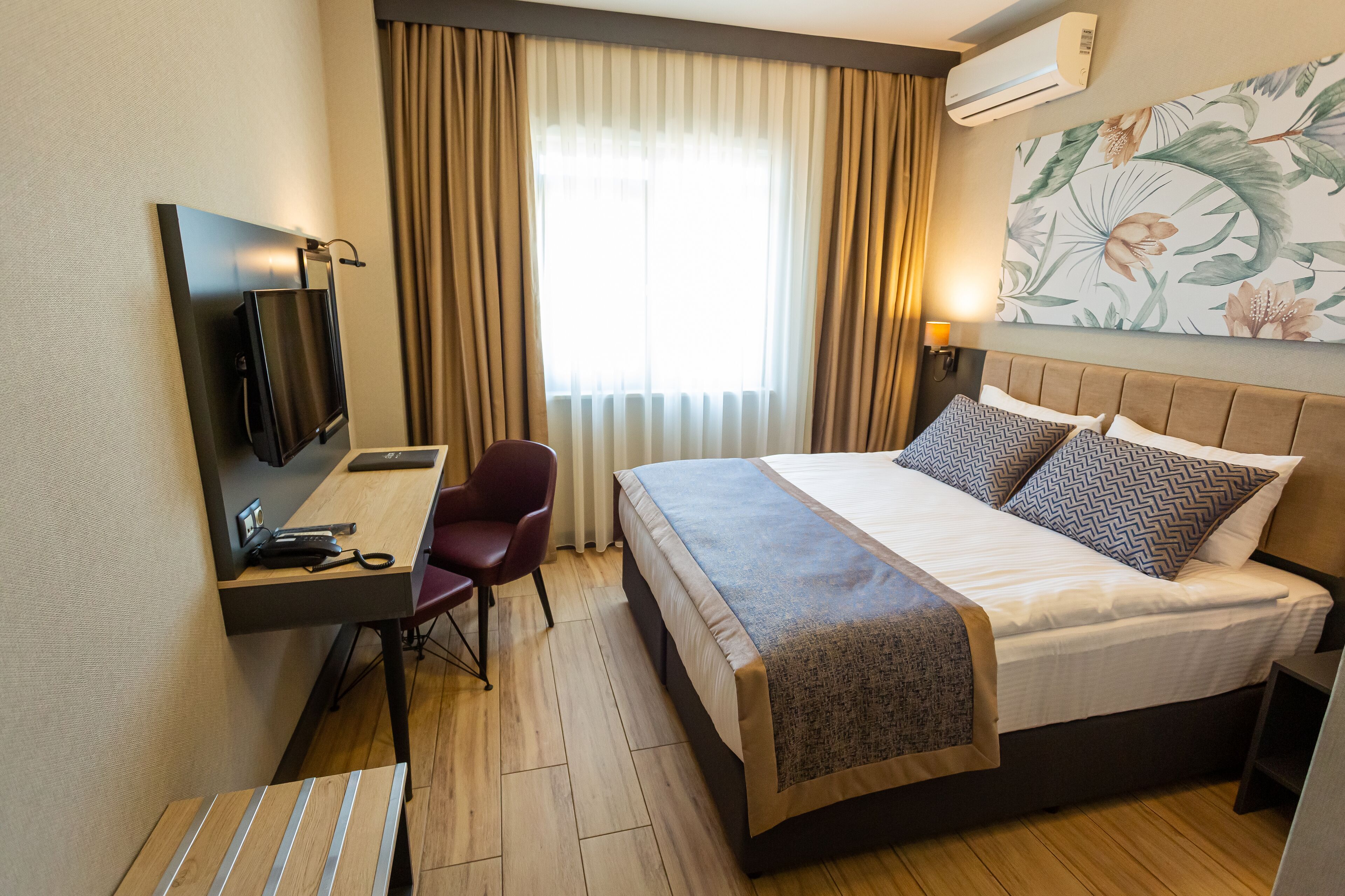 Una habitación de hotel con cama, escritorio, silla, televisor y ventana con cortinas.