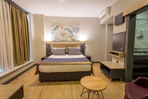 A modern hotel room with a large bed, a small round table, a red chair, a wooden bench, and a large window with curtains. - Levor Hotel (Bursa)