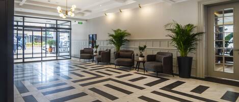 A spacious lobby with a geometric patterned floor, comfortable seating, and potted plants.