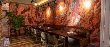 A restaurant with wooden flooring, a large mural on the wall, and a seating area with tables and chairs.