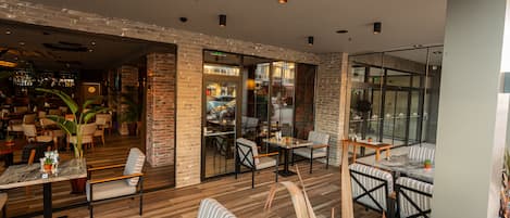 A modern restaurant with brick walls, wooden flooring, and a mix of seating options including tables, chairs, and a sofa.