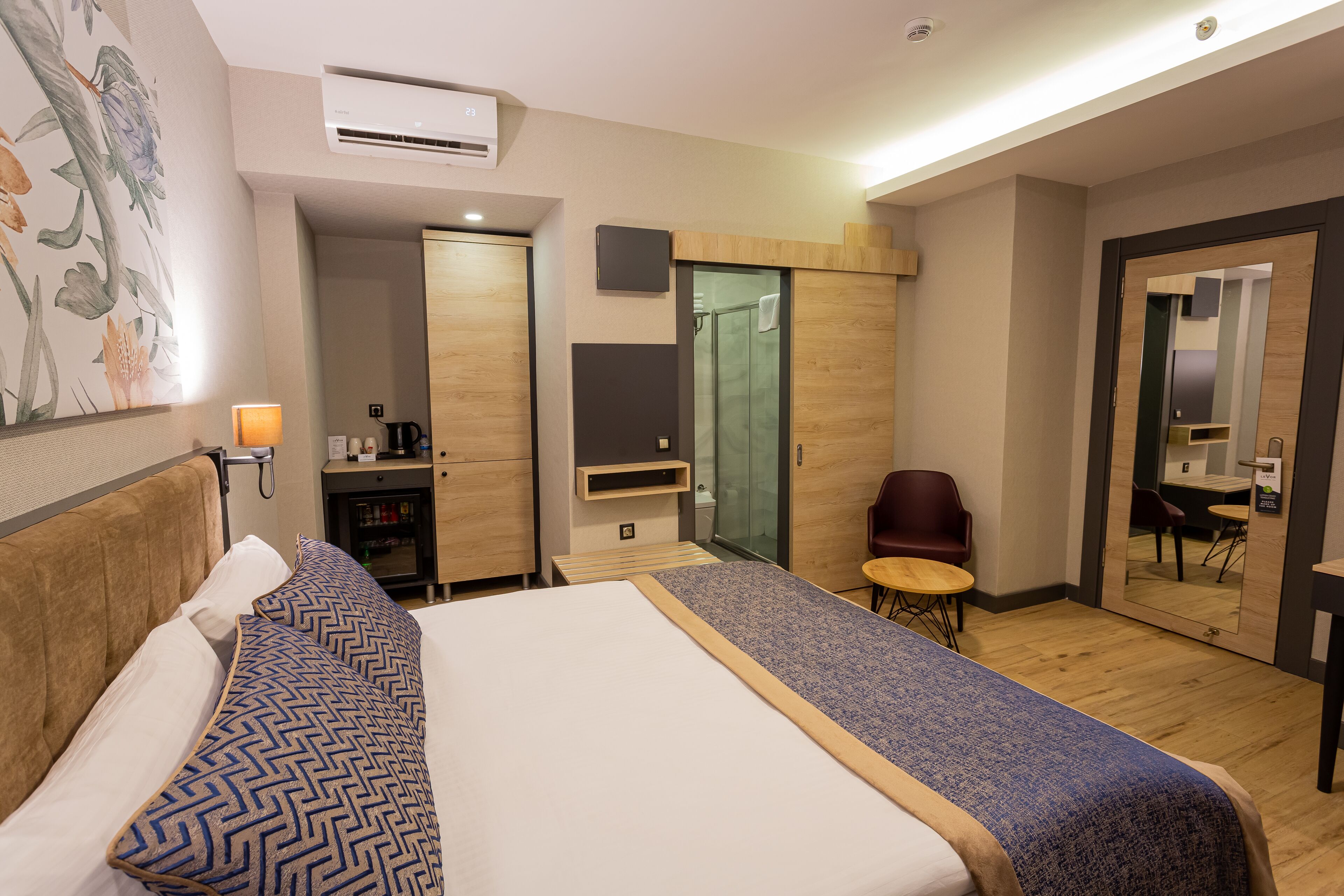 Une chambre d’hôtel comprenant un lit, un bureau, une chaise, une petite table, un miroir et une armoire.
