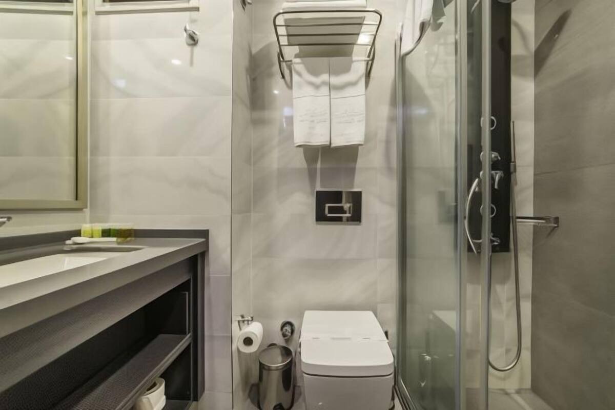Un baño moderno con cabina de ducha de vidrio, inodoro, lavabo con espejo y toallero.