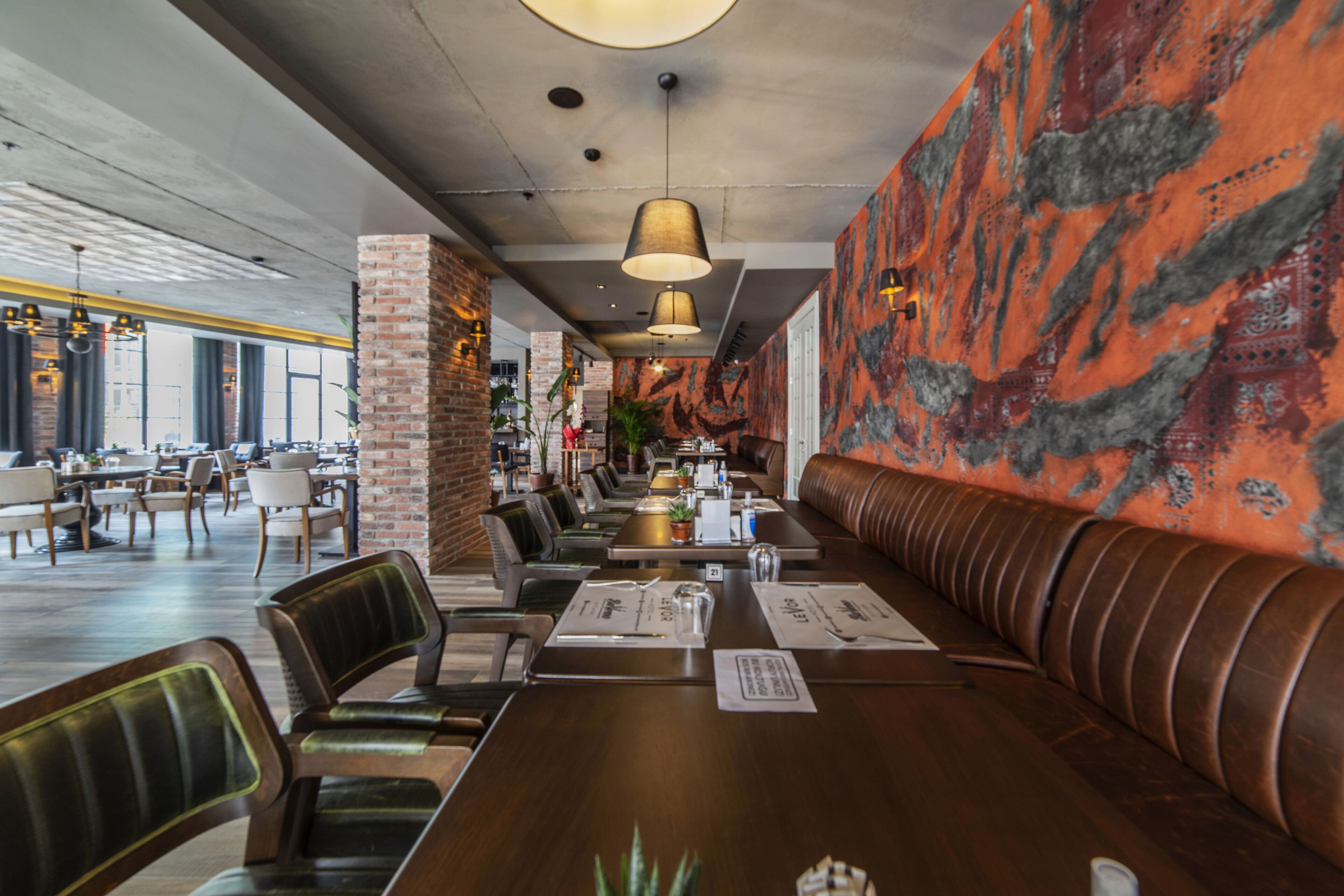 A restaurant with a long wooden table, leather booth seating, and hanging pendant lights.